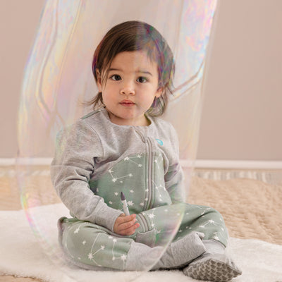 Child wearing a green and gray onesie with star pattern in a crib.